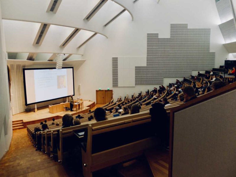University lecture hall with a lecturer speaking on a stage at the front