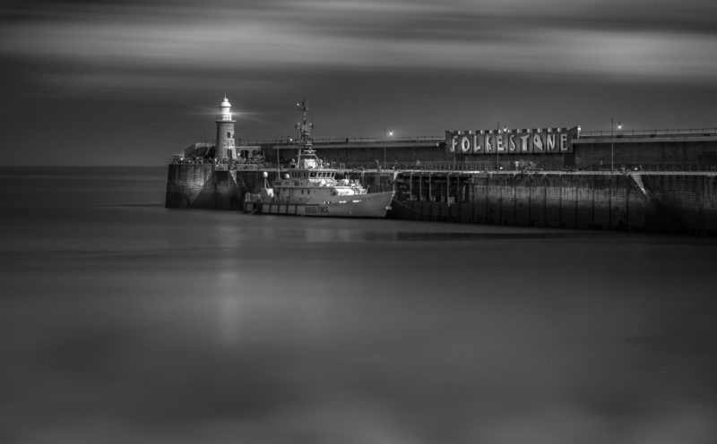 Black and white image of Folkestone Harbour with a Border Force patrol boat