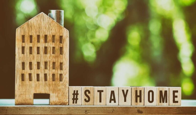 Wooden model house with the words #StayHome in wooden blocks beside it