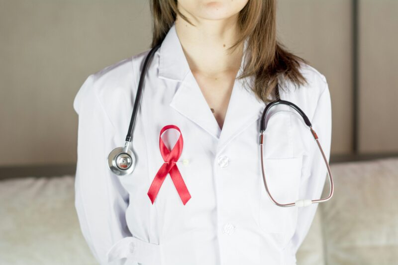 a female doctor wearing a white coat and red AIDs awareness ribbon